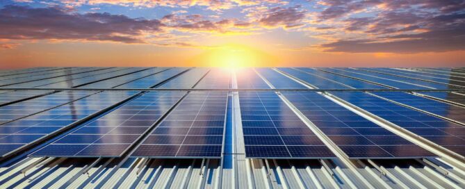 Fotovoltaické panely na střeše firemního objektu při západu slunce.