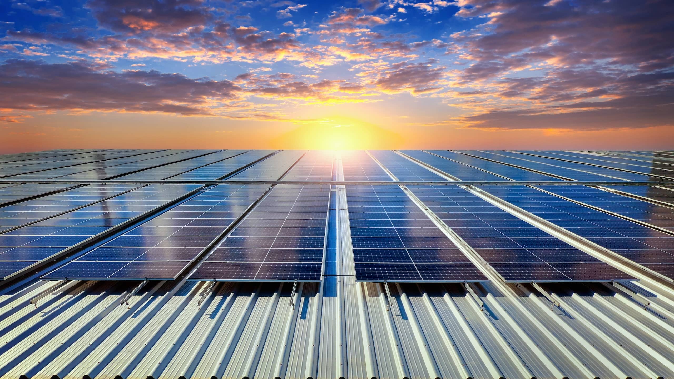 Fotovoltaické panely na střeše firemního objektu při západu slunce.